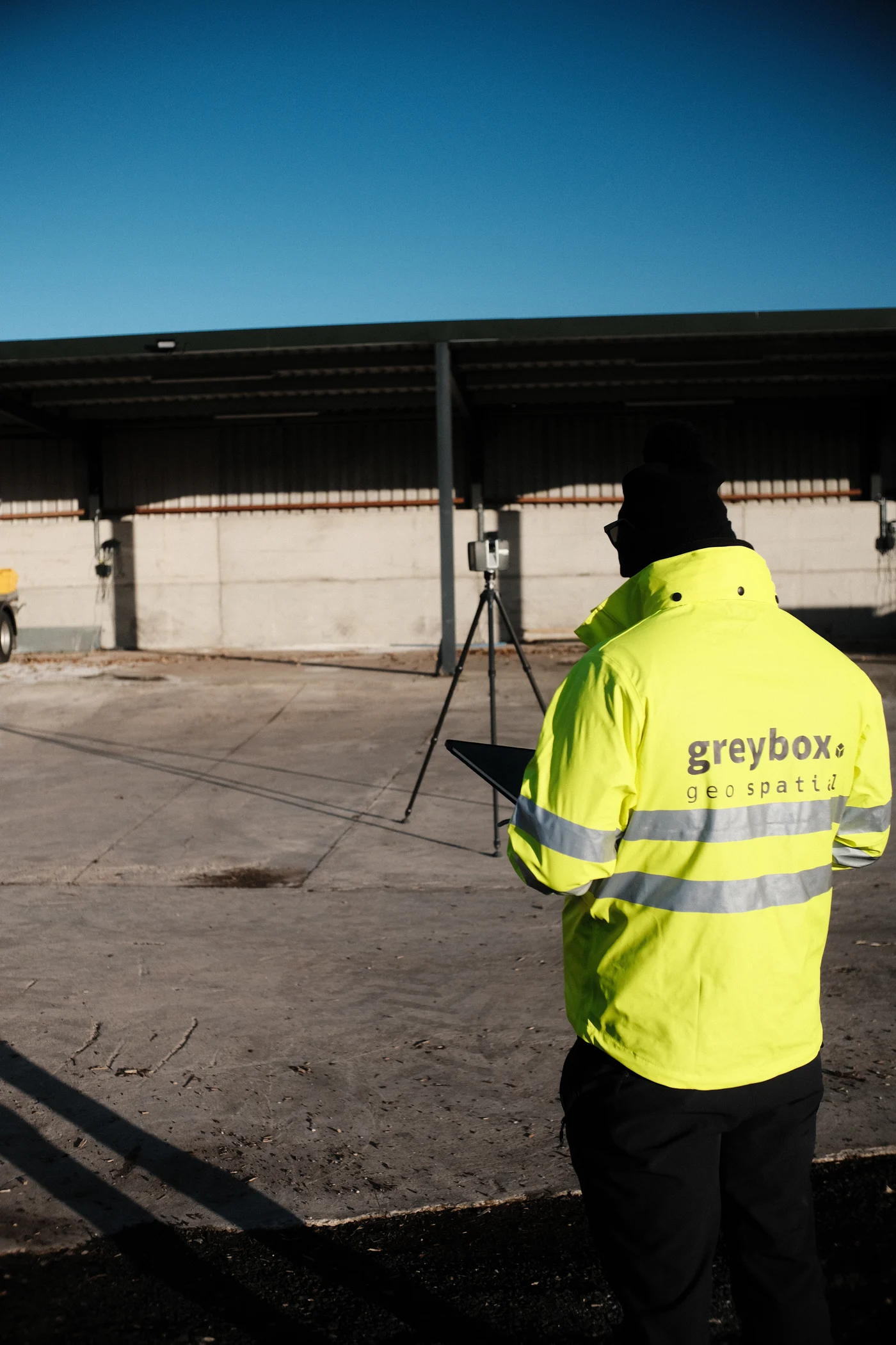 Greybox surveyor in branded hi-vis reviewing capture data beside a terrestrial laser scanner